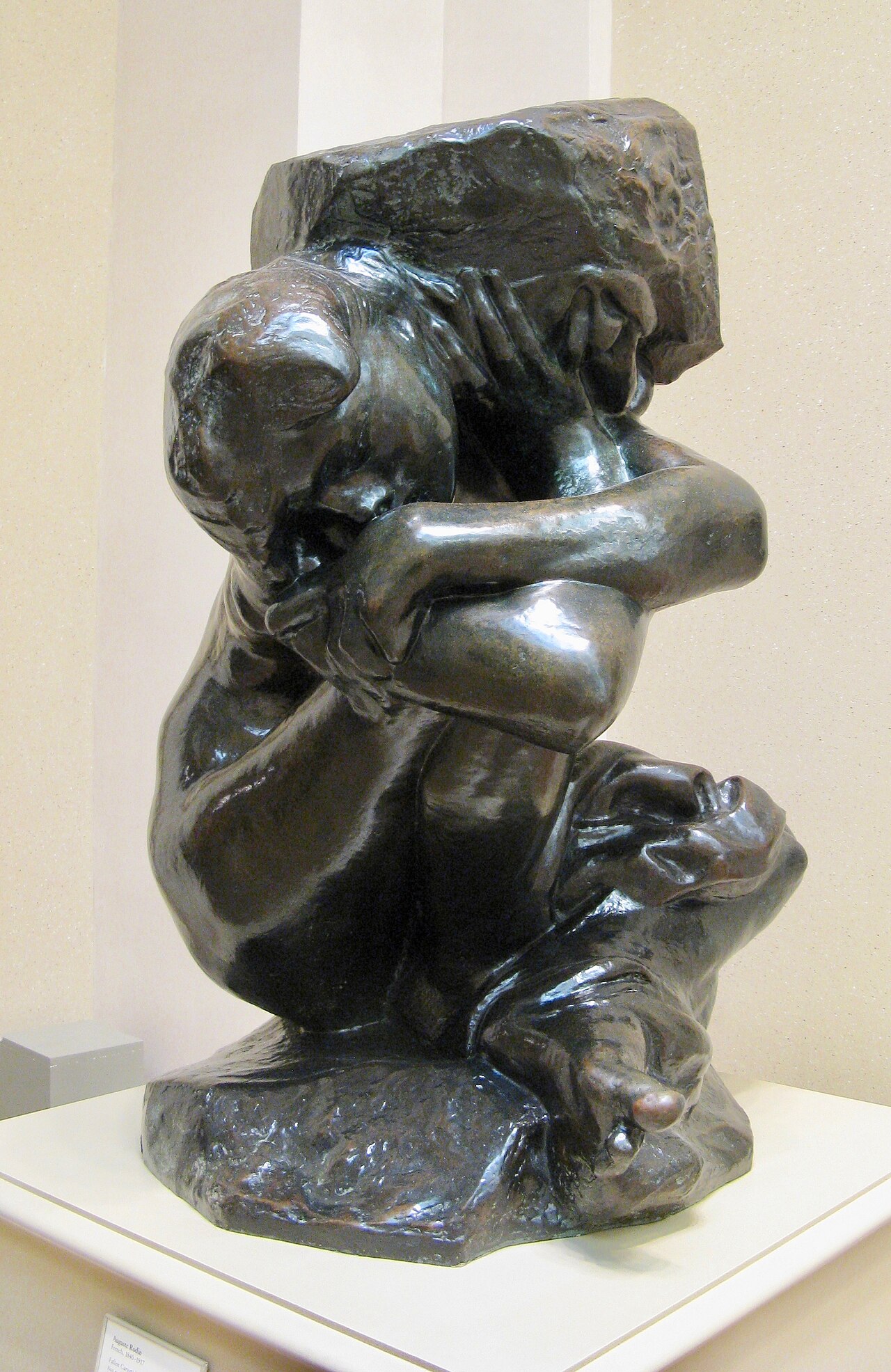 A crouching nude figure crushed under a massive stone block, muscles straining, still carrying the weight